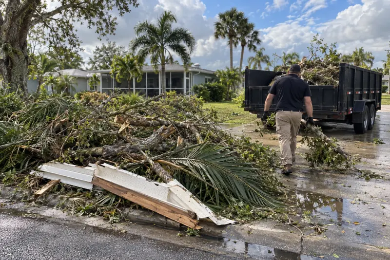 Storm debris, palm fronds and broken soffit piled at a Florida curb beside a dump trailer